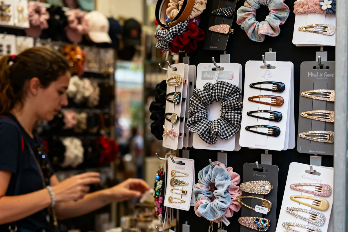 Femme choisissant des accessoires capillaires, serre-têtes et barrettes colorées dans un présentoir de magasin.