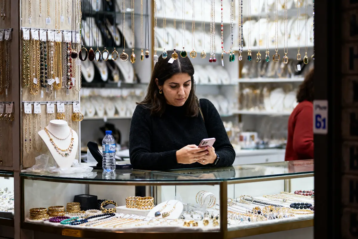 Femme utilisant un smartphone dans une bijouterie, entourée de colliers et bracelets exposés.