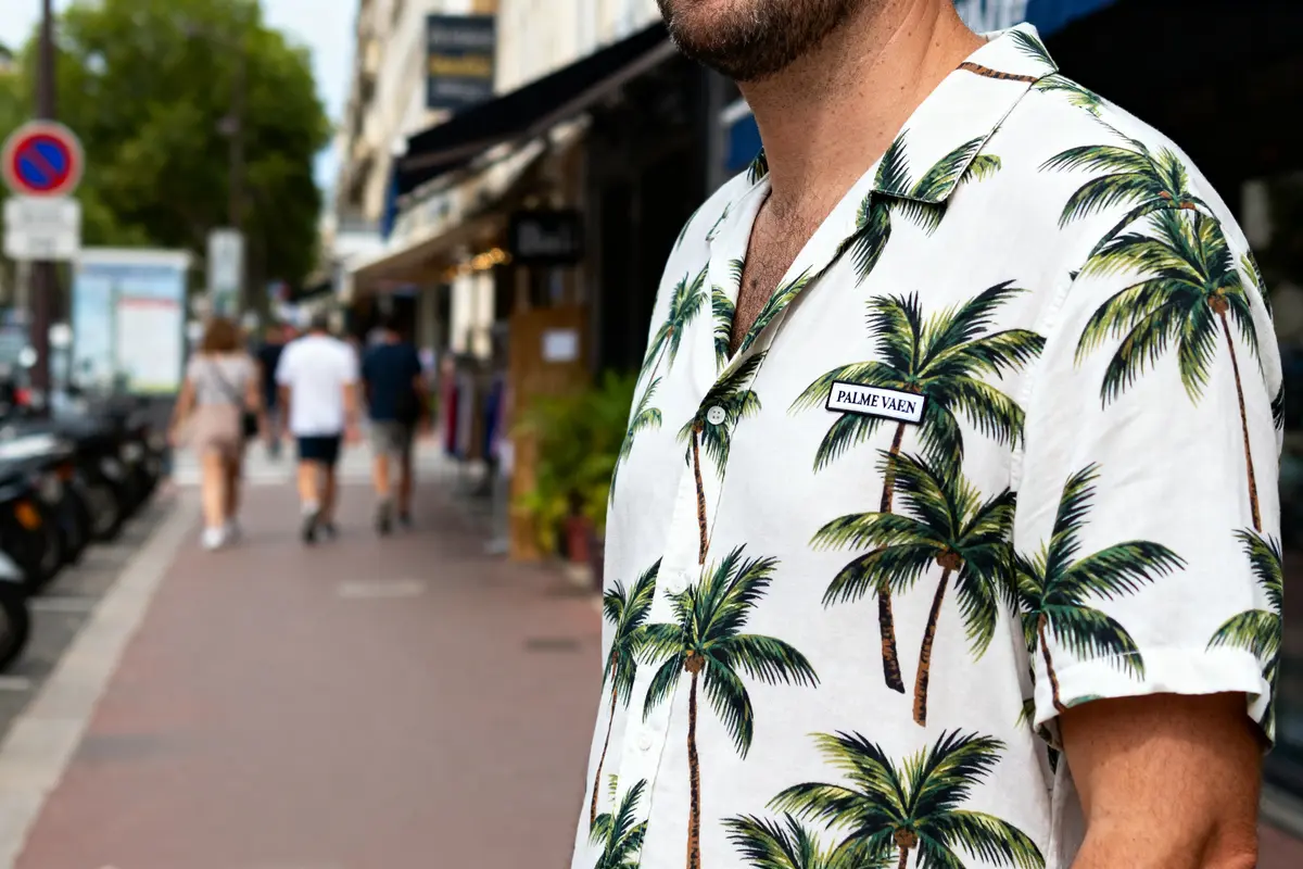 Homme en chemise imprimée palmiers, marchant dans une rue urbaine animée par plusieurs passants flous.