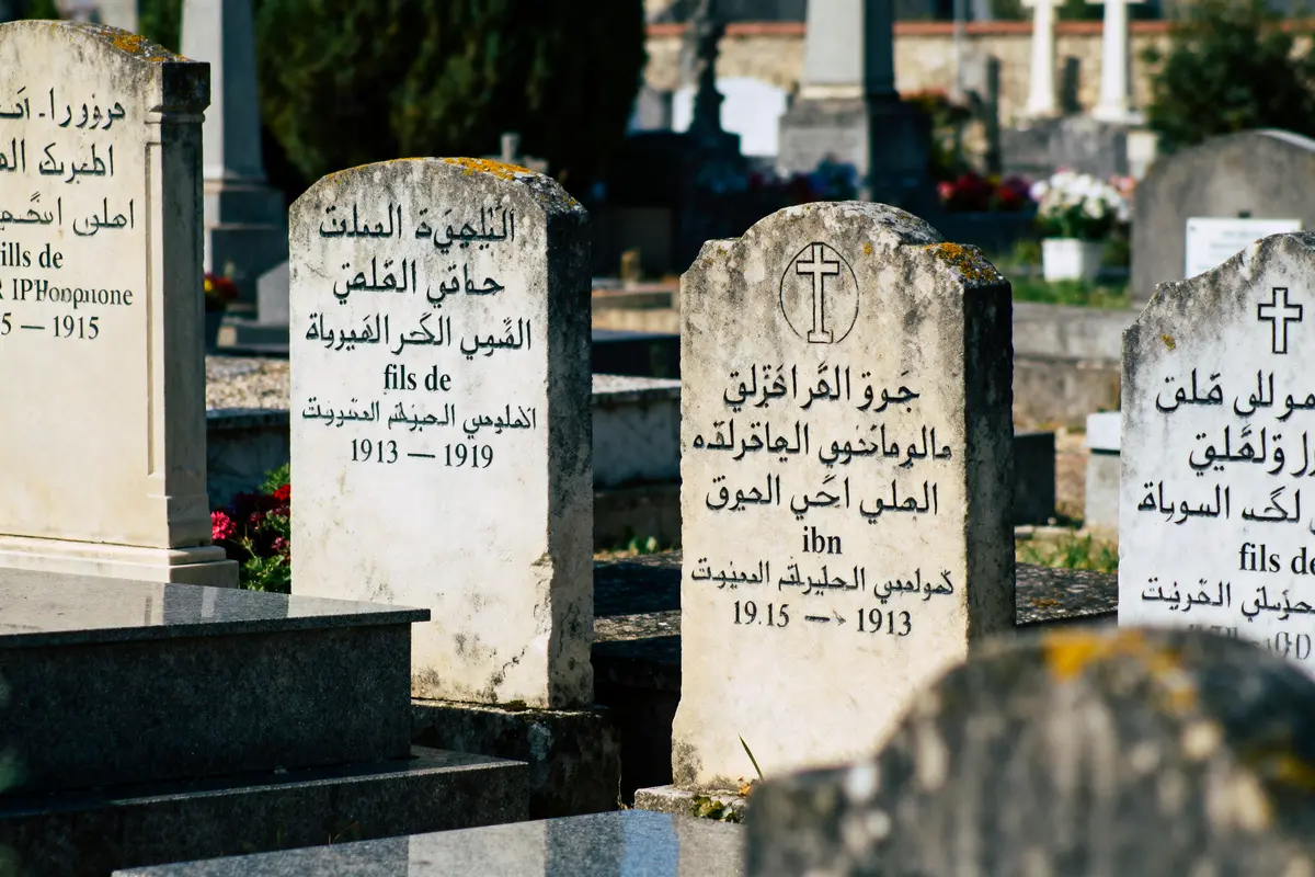 Vieilles pierres tombales avec inscriptions en plusieurs langues dans un cimetière ensoleillé.